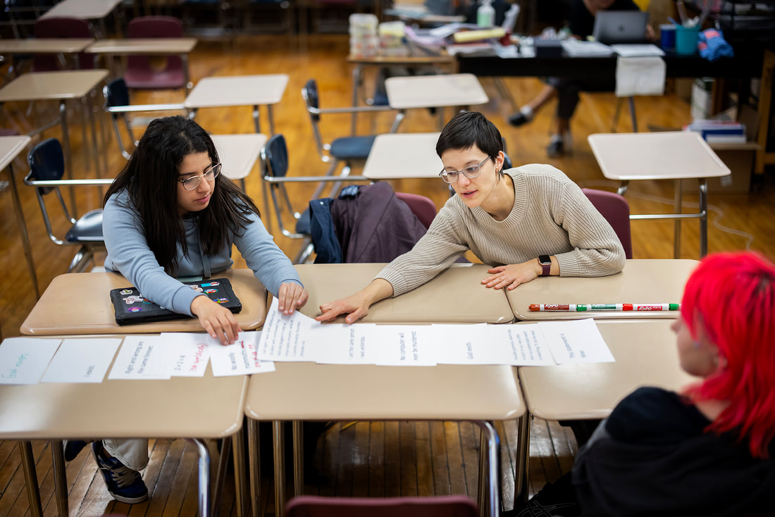 Photo of Jacqui sitting with two students, working on a philosophical activity about certainty.